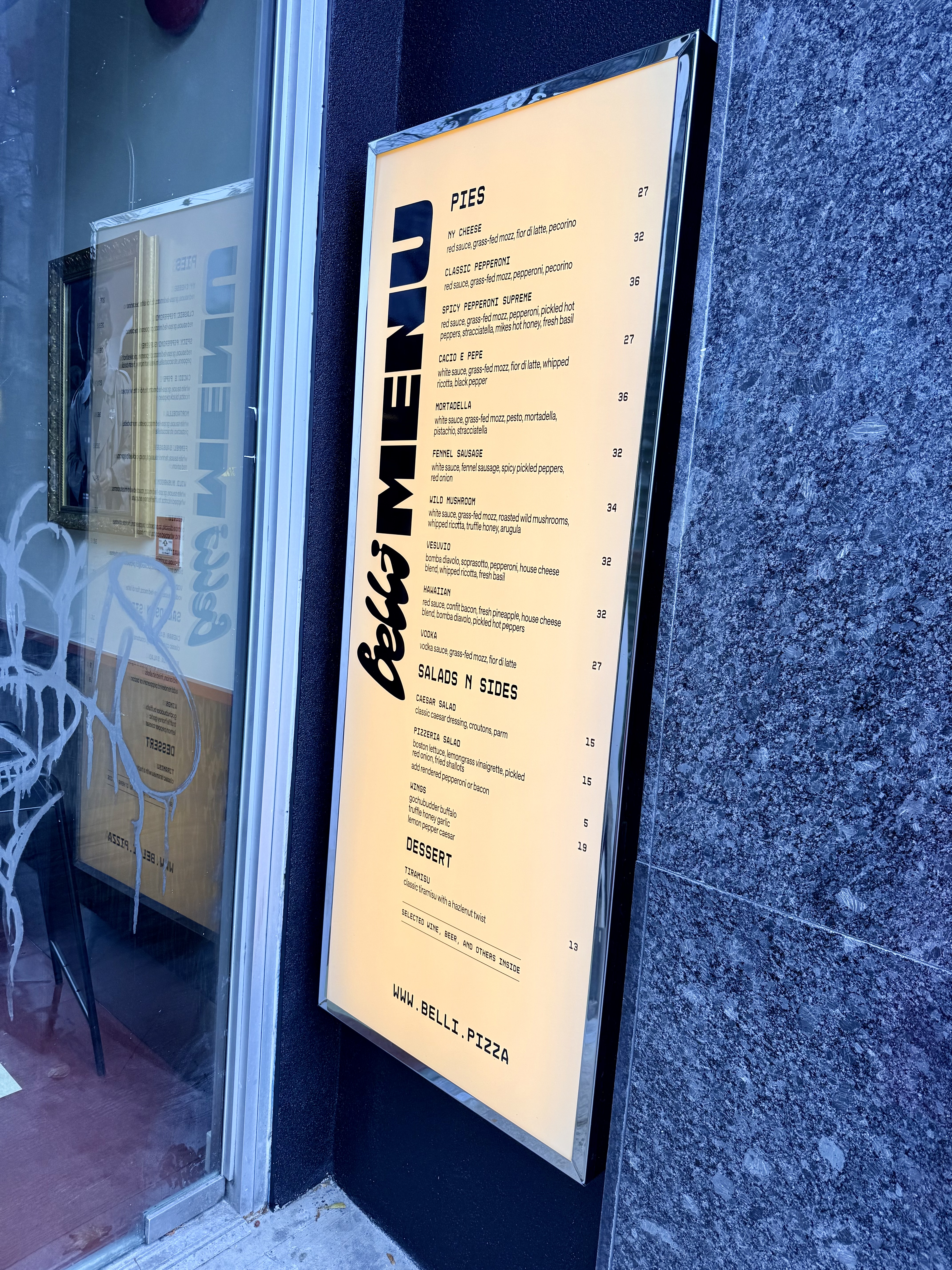Picture of the Belli Pizza entranceway, they have a menu outside the door. There is some graffiti on their glass doors.