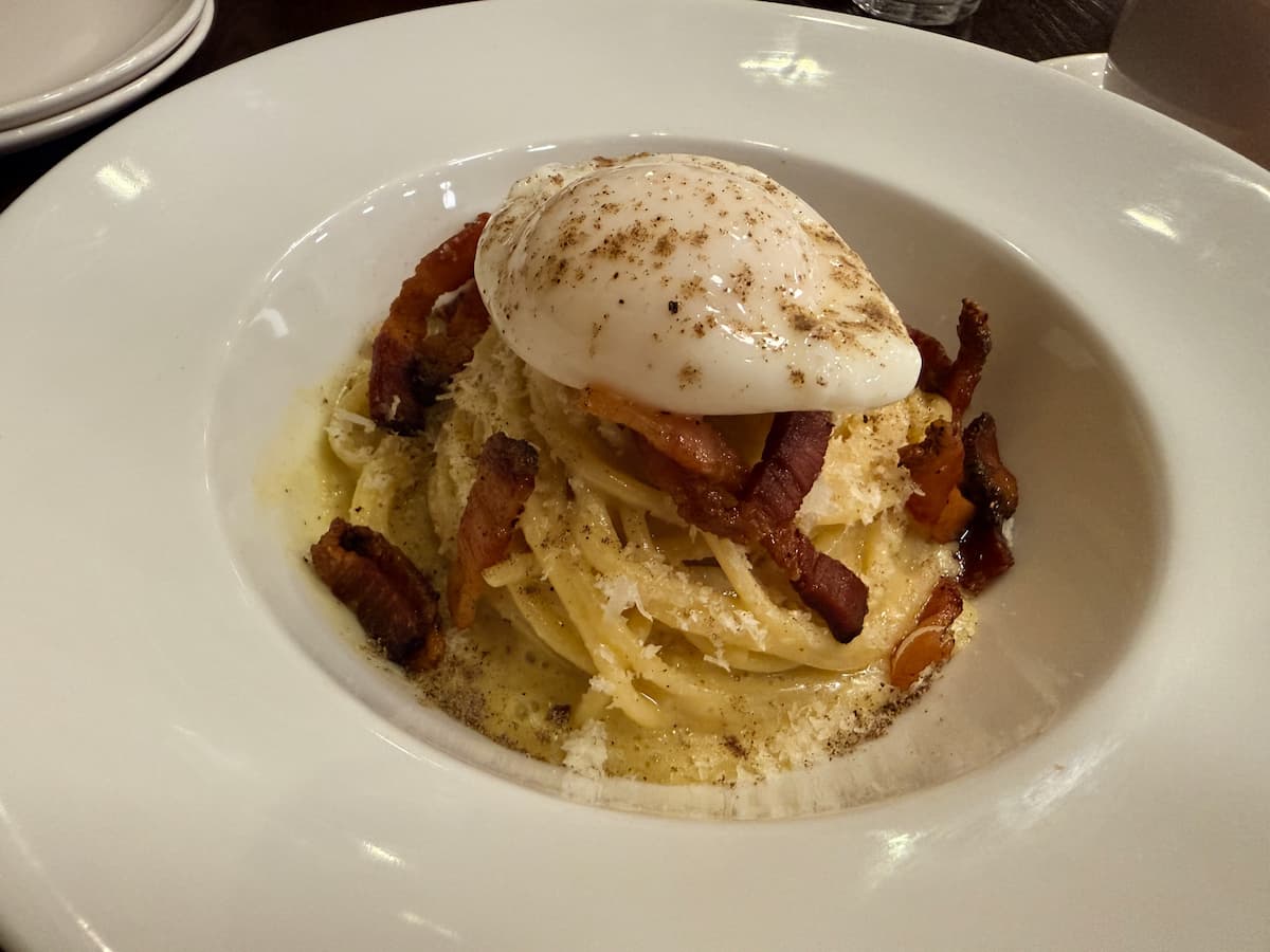 A twirled pile of spaghetti with crispy lardons of guanciale, sprinkled cheese, and a poached egg on top.
