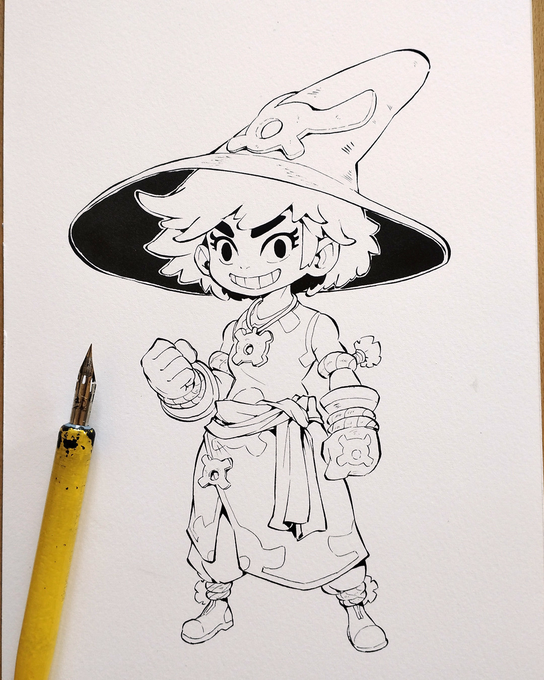 Illustration of a cartoon witch character in black ink, standing with a determined expression and clenched fist, wearing a wide-brimmed hat. A yellow dip pen rests on the left.