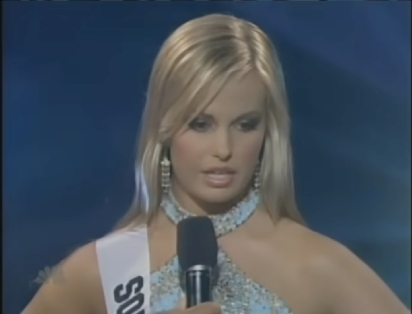 A blonde pageant contestant stares past a microphone