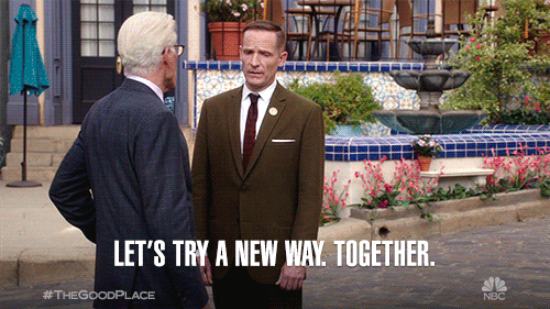 A man in suit and bowtie (Michael from The Good Place) lays his hand on the shoulder of a man in a brown suit with a red tie (Shawn) and says: Let's try a new way, together.