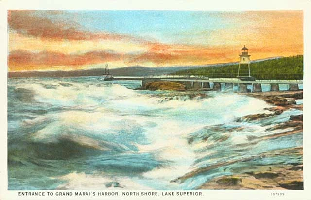 A postcard of a watercolor of waves washing up on the Grand Marais shoreline with the lighthouse in the painting.
