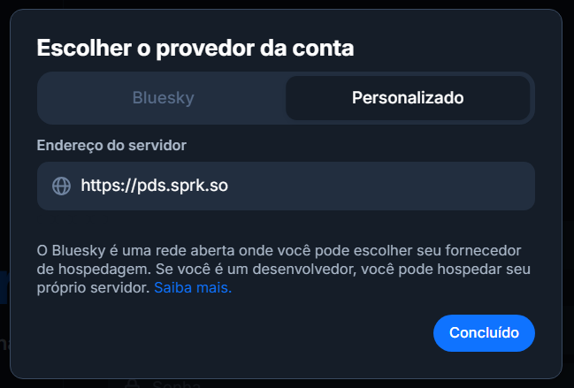 Pop-up para Escolher o provedor da conta, com duas abas: Bluesky e Personalizado.
A aba Personalizado está selecionada, exibindo o campo de Endereço do servidor preenchido com https://pds.sprk.so.
Botão Concluído.