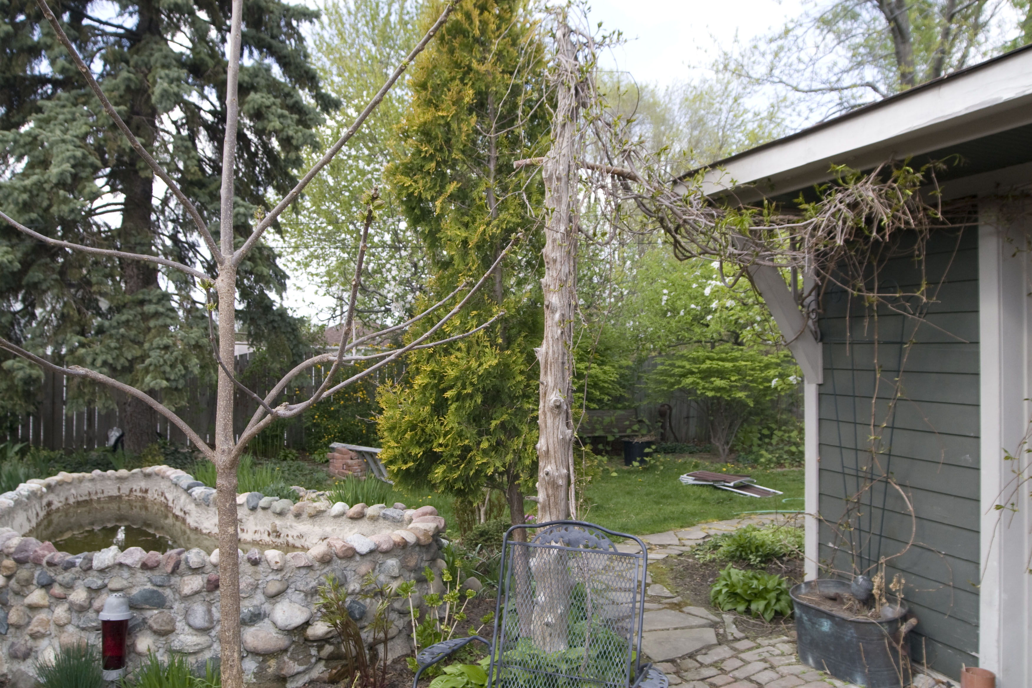 A very well landscaped backyard, with a pond made of rocks, several trees, and cobbled pathways leading away from the camera