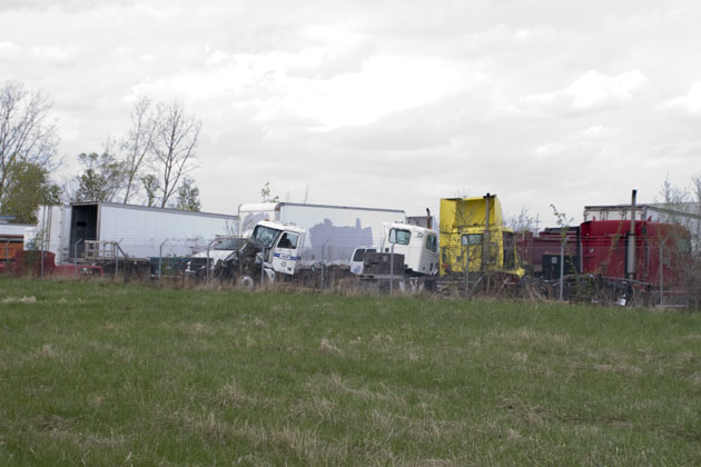 A bunch of broken down old semi trucks and tractor trailers in total disrepair behind an ugly chain link fence topped with razor wire.