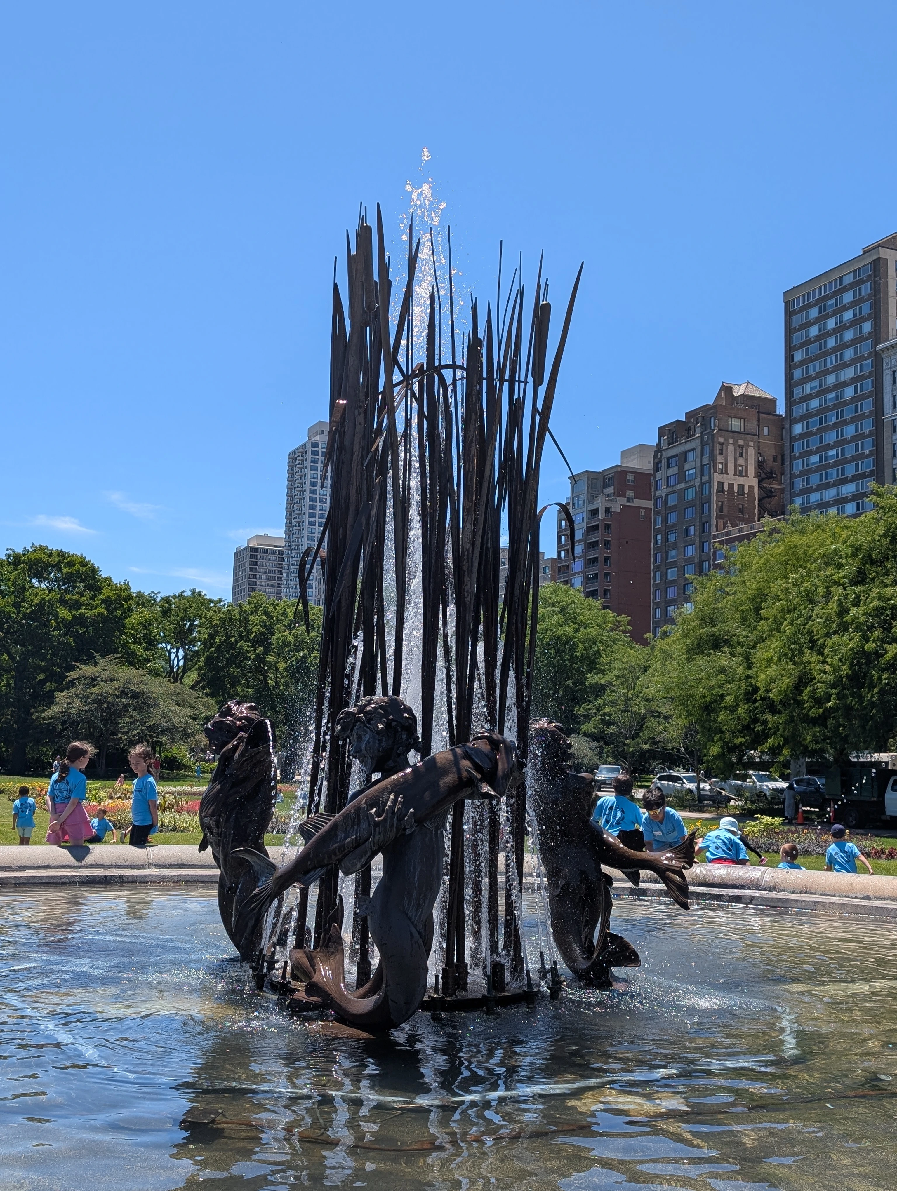 A sculpture at the center of the fountain. It features a stabby-looking array of metal pointy things--oh, wait, those are cattails--surrounded by a ring of mermaid-cherubs cradling large fish.