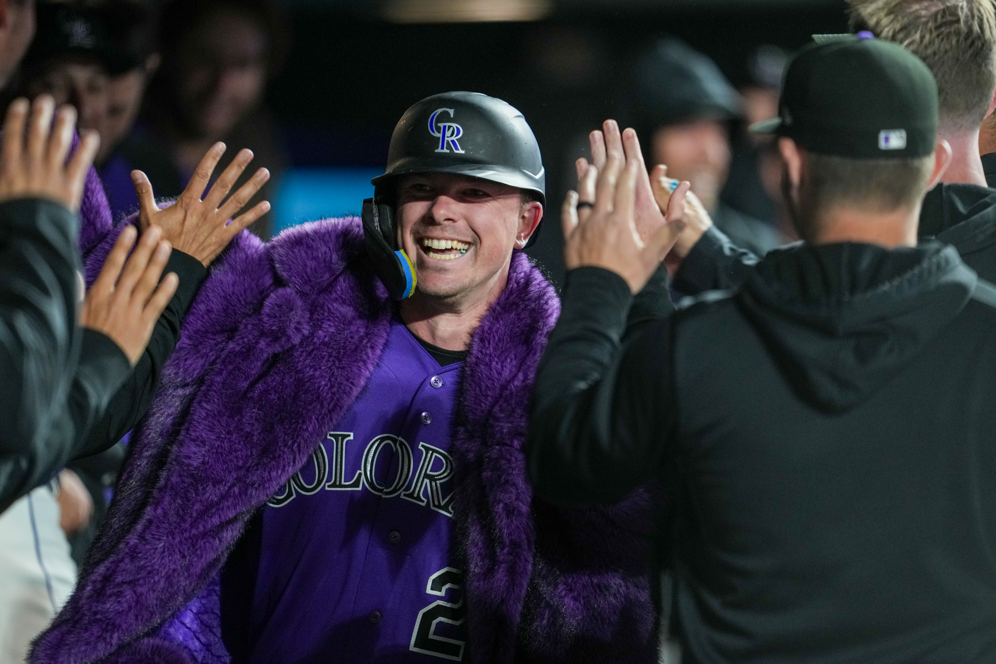 Troy Johnston high fives teammates in the dugout while wearing the Rockies new purple home run coat.
