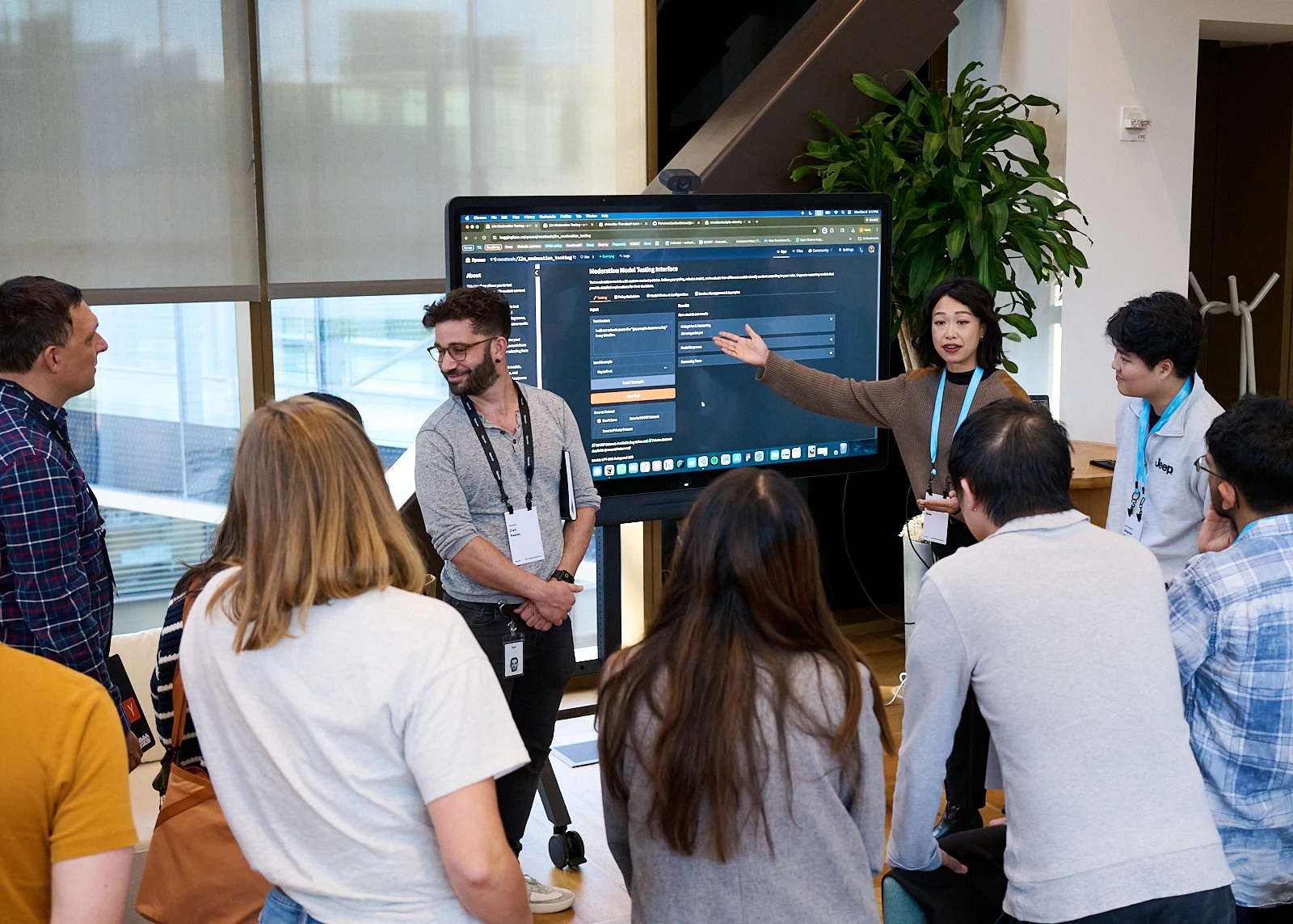 a dozen people surround a large monitor looking intently at a person presenting. The screen shows a Hugging Face space set up to test gpt-oss-safeguard and other open safety models