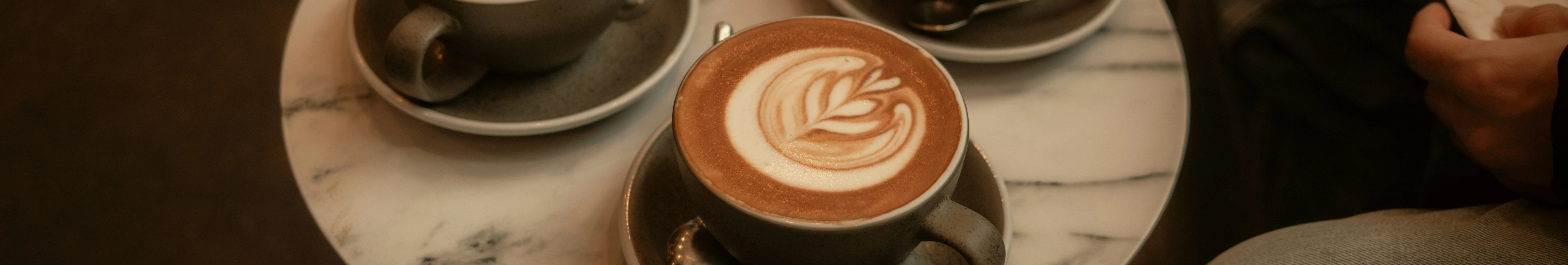 Latte art in a green ceramic mug sits on a marble white-gray circle table. Two mugs are in the background.

Photo by Bryan Brittos from Unsplash.