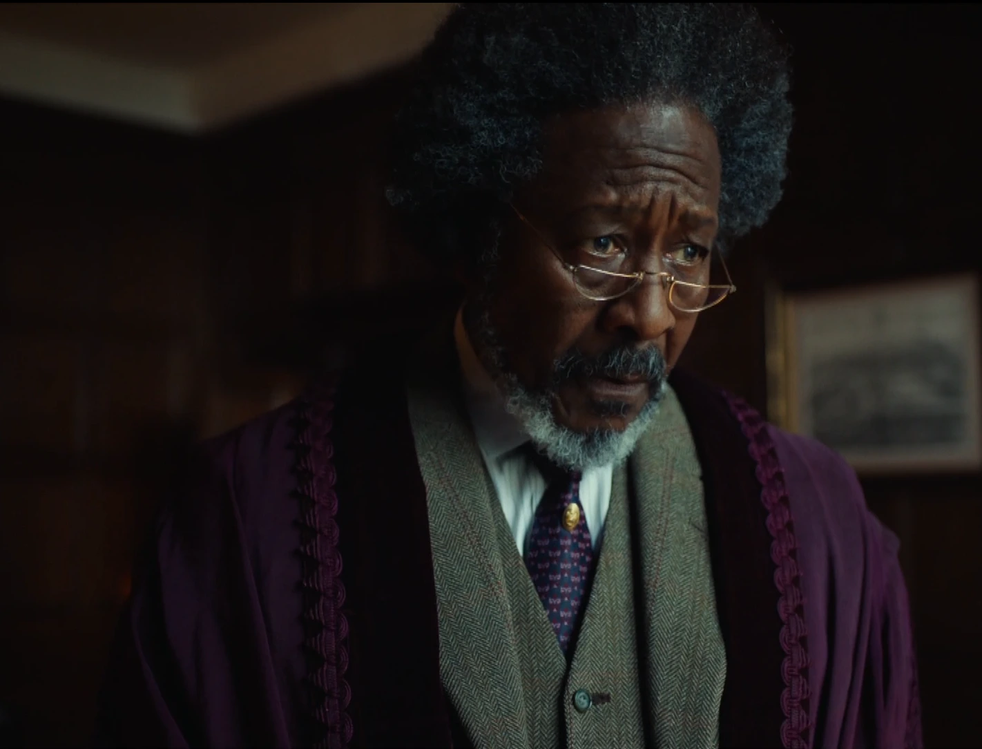 Le Maître de Jordan College, interprété par Clarke Peters, homme noir d'une soixantaine d'années, aux longs cheveux gris et crépus, aux yeux noirs, à la barbe noire blanchissant sous l'effet de l'âge, avec des lunettes en demi-lunes sous les yeux, portant une veste violette, sous laquelle on distingue un costume gris, une chemise claire et une cravate violette. Il porte le regard vers quelque chose de lointain, ayant l'air songeur.
On distingue un intérieur avec plusieurs boiseries en arrière-plan, ainsi qu'un cadre doré, indiquant une pièce richement décorée.