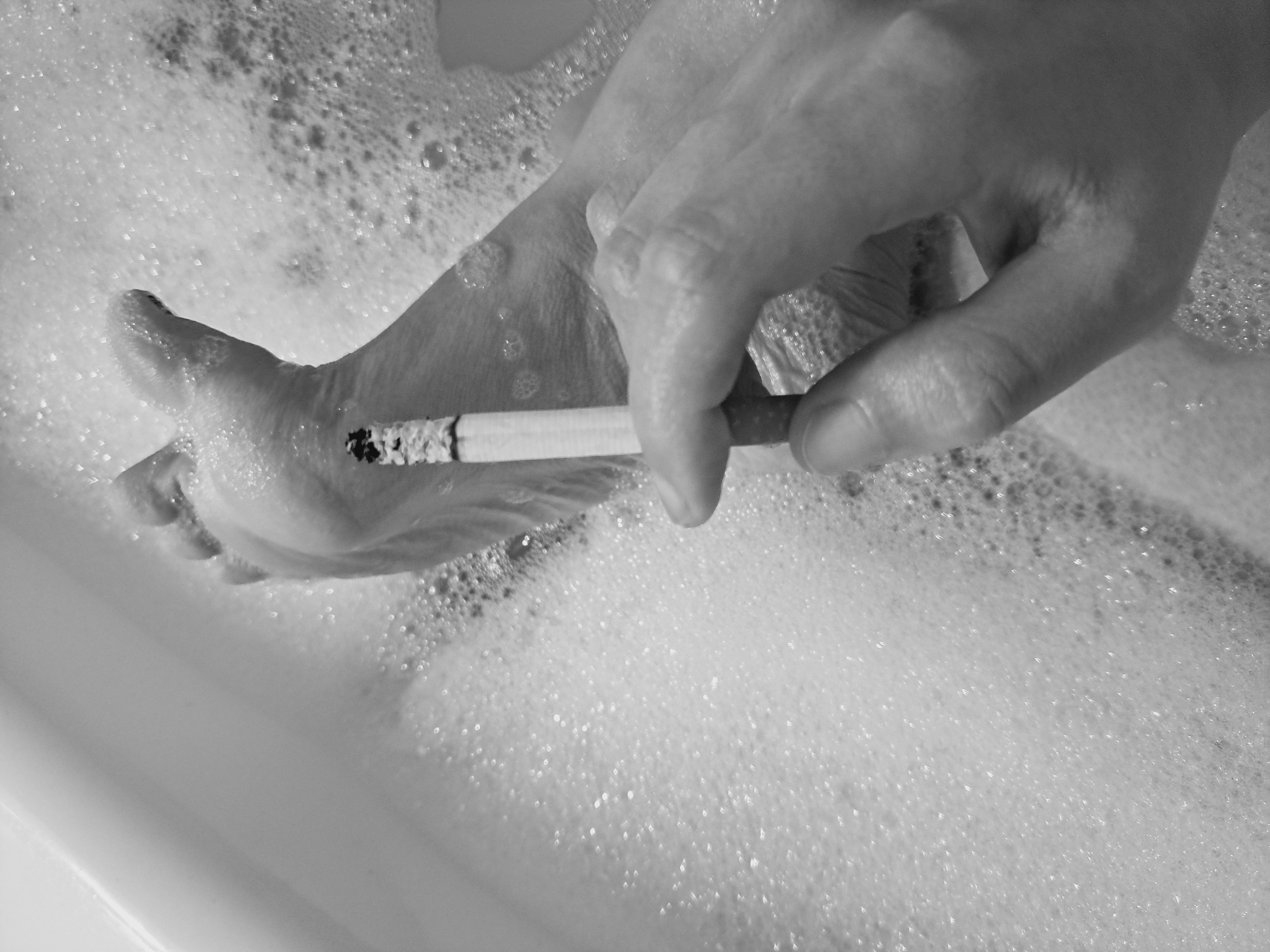 Valerie Rayne takes a black and white photo showing off her wrinkled toes and soles covered in bubbles while she holds a cork-filtered cigarette between her index and middle fingers.