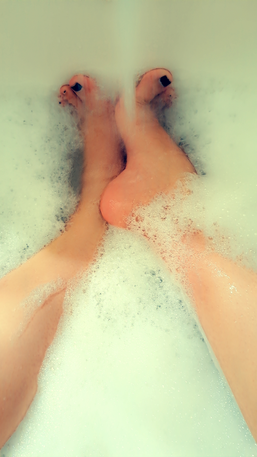 Valerie Rayne shows off her feet under flowing water from the faucet with black painted toenails and her high arches in a very bubbly bath.