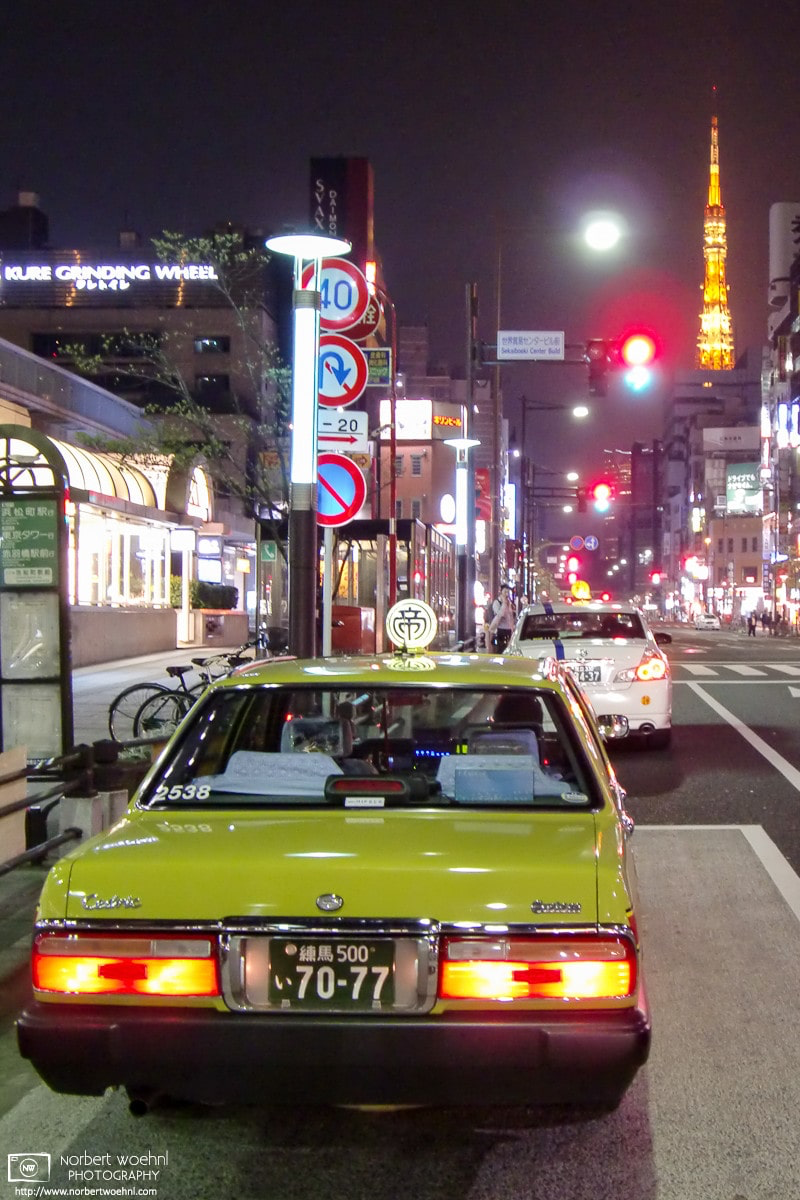 Outside Hamamatsucho Station in Tokyo, Japan, an old-school taxi looks ready for a ride that is headed towards the illuminated Tokyo Tower in the background. © 2009 Norbert Woehnl Photography.