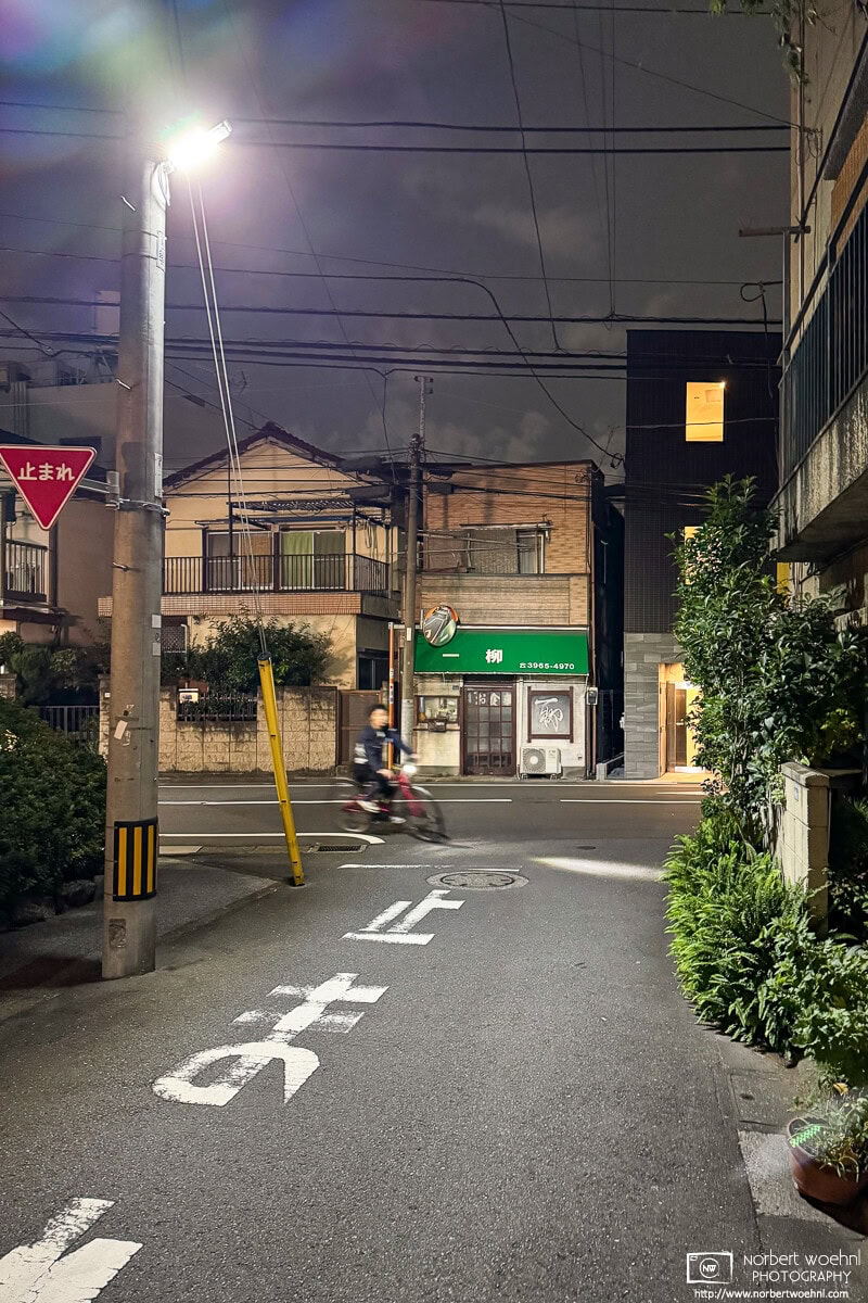 A bicyclist is turning the corner in this night photograph from the Hasunumacho district of Itabashi Ward of Tokyo, Japan. © 2025 Norbert Woehnl Photography.