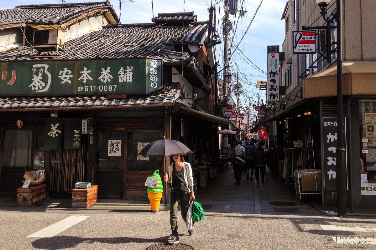 On a summer day in the Fushimi Ward of Kyoto, Japan, a woman carrying a parasol crosses the street outside an old tea store. © 2014 Norbert Woehnl Photography.