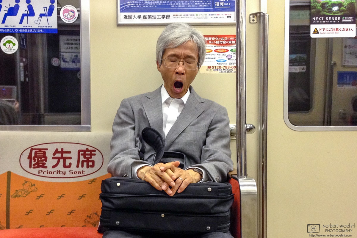 A tired man with a business bag is seated on a subway seat in Fukuoka, Japan. © 2015 Norbert Woehnl Photography.