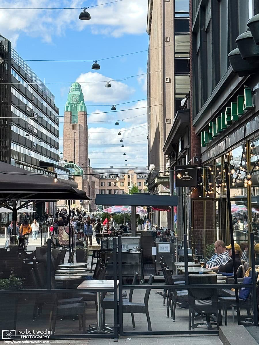 The clock tower (kellotorni) of Helsinki Central Station makes an appearance behind shops and restaurants in the Kluuvi district of Helsinki, Finland. © 2026 Norbert Woehnl Photography.