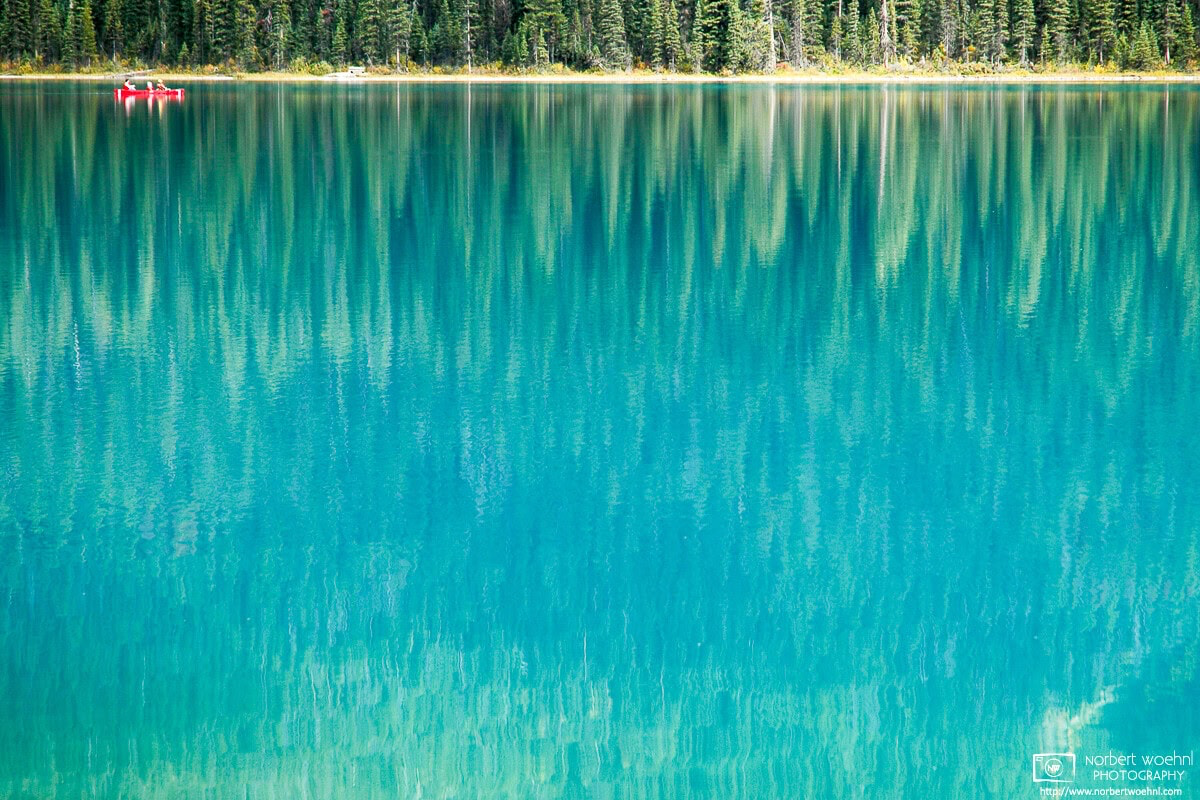 A canoe is moving on turquoise-blue Emerald Lake in Yoho National Park in the Canadian Rockies. The lake reflects the adjacent forest of spruce trees. © 2005 Norbert Woehnl Photography.