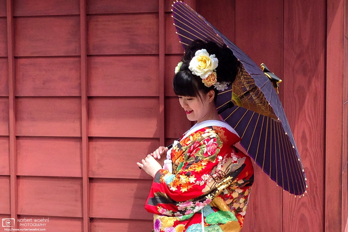 A young woman in kimono and holding a Japanese paper umbrella is posing outside a historic building in Kanazawa, Japan. © 2015 Norbert Woehnl Photography.