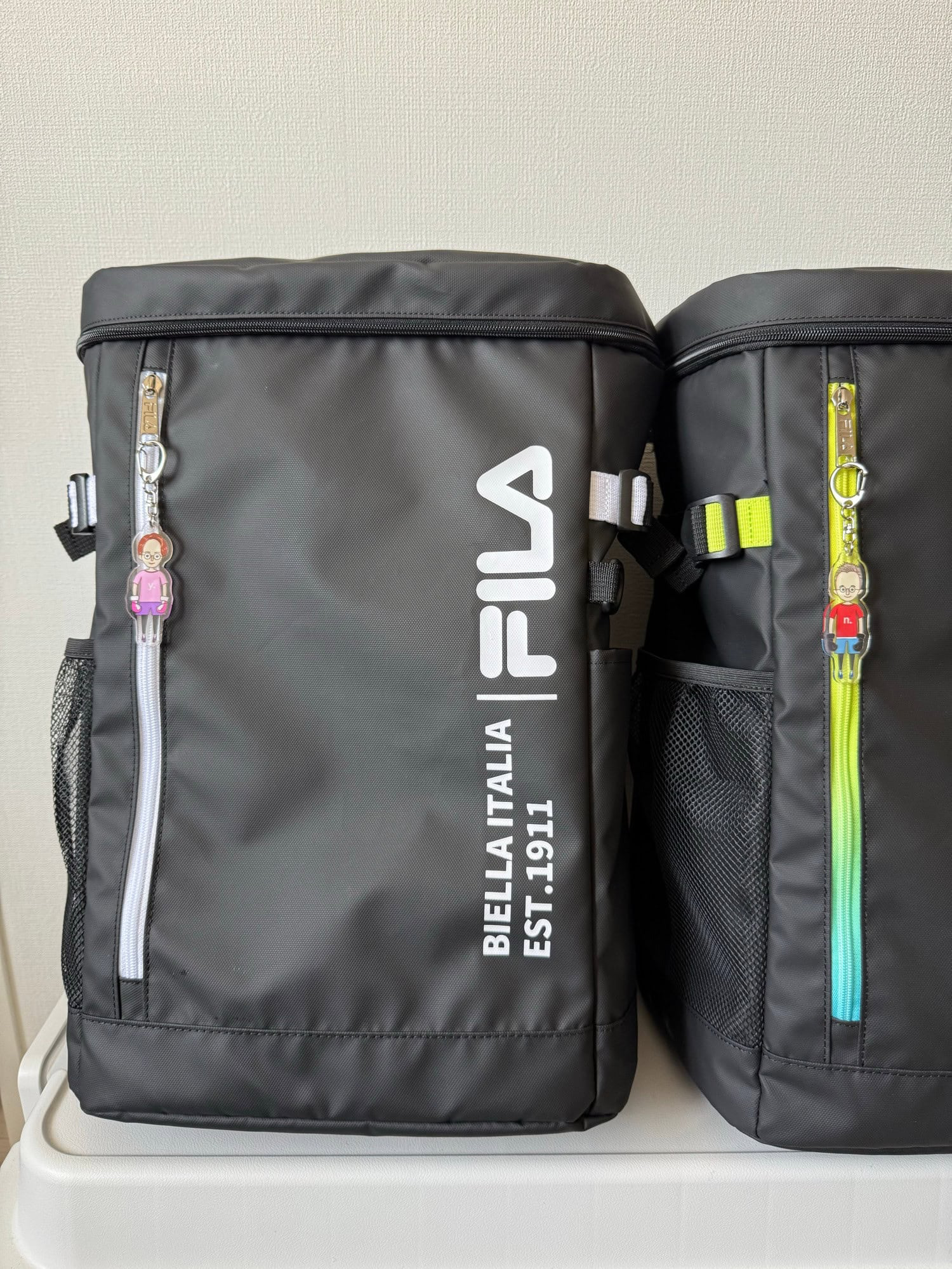 Two key rings with illustrations of a male and a female character in kickboxing sports gear, attached to zippers on two sports bags. © 2025 Norbert Woehnl Photography.