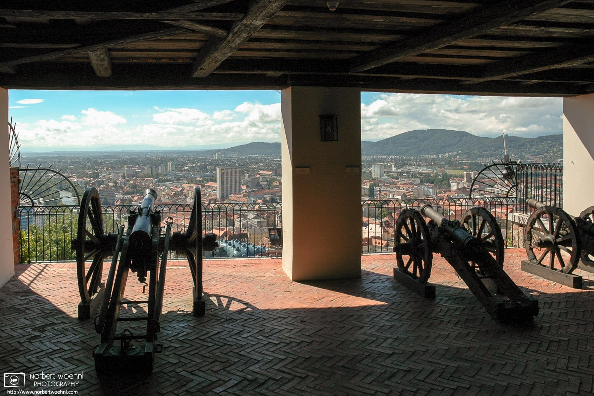 Cannons at the Schlossberg Bastion in Graz, Austria, opening up a view towards the historic city center which is a UNESCO World Heritage site. © 2004 Norbert Woehnl Photography.