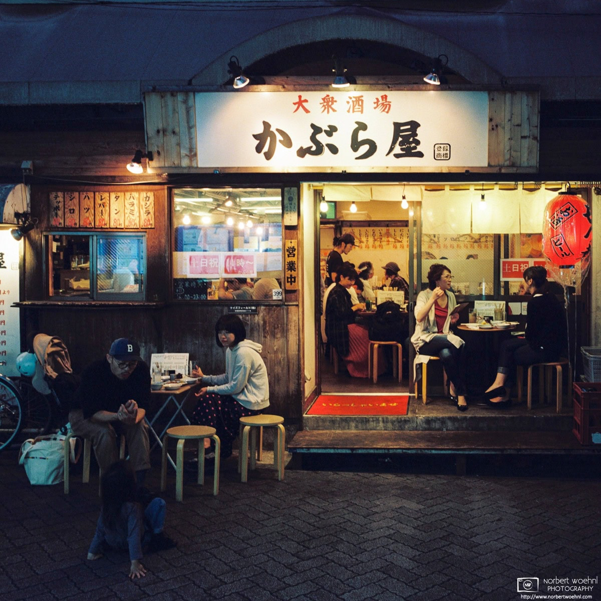 Evening life at an Izakaya (Japanese pub) in the Asagaya area of Tokyo, Japan. People are casually chatting and playing with their kids. © 2019 Norbert Woehnl Photography.