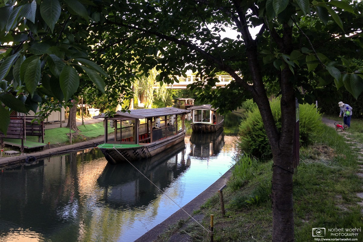 Boats are tied on a canal in the Fushimi Ward of Kyoto, Japan, while a woman walks her dog along the embankment. © 2014 Norbert Woehnl Photography.