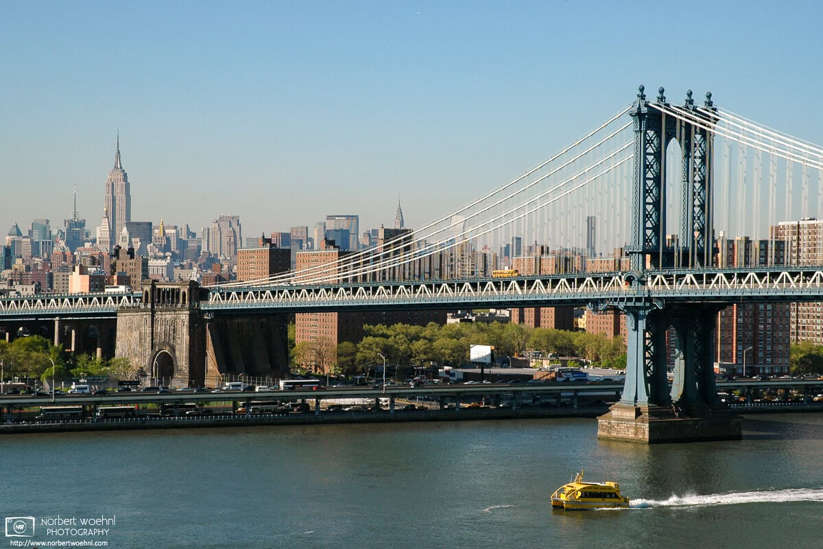 A water taxi is speeding along the East River in New York City. Manhattan Bridge and the Empire State Building are visible in the background. © 2005 Norbert Woehnl Photography.