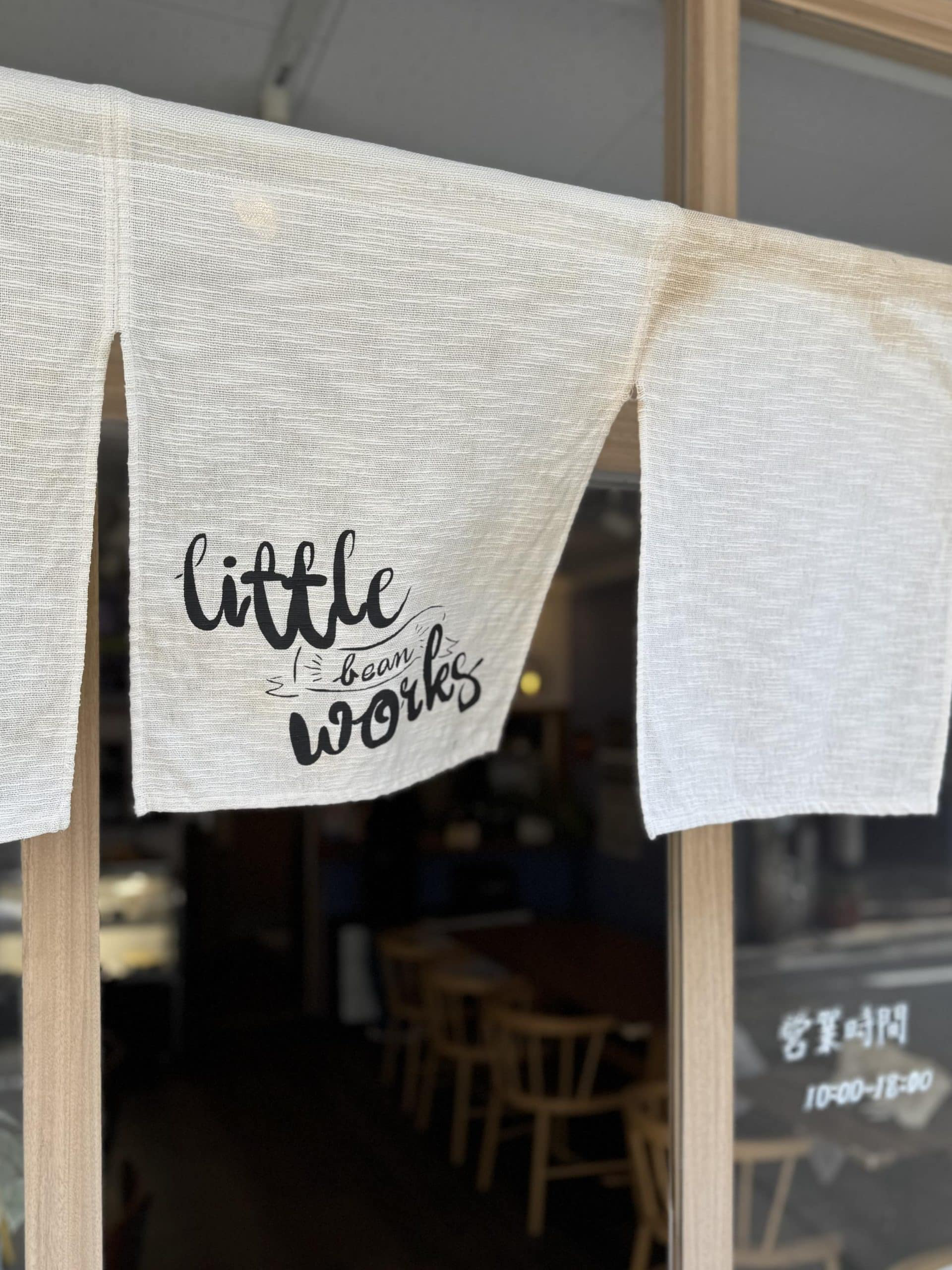 Noren (fabric divider) with shop logo hung at the entrance to "Little Bean Works", a cafe in the Itabashi Ward of Tokyo, Japan. © 2026 Norbert Woehnl Photography.