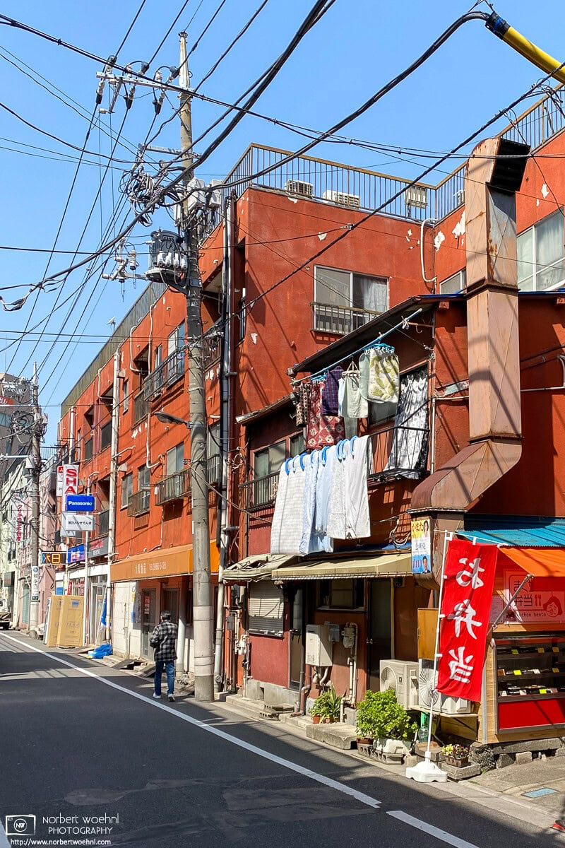 Colorful scene on a backstreet in the Itabashi Ward of Tokyo, Japan. In front a bento shop and laundry day, further back some boxes outside an electronics store. © 2021 Norbert Woehnl Photography.