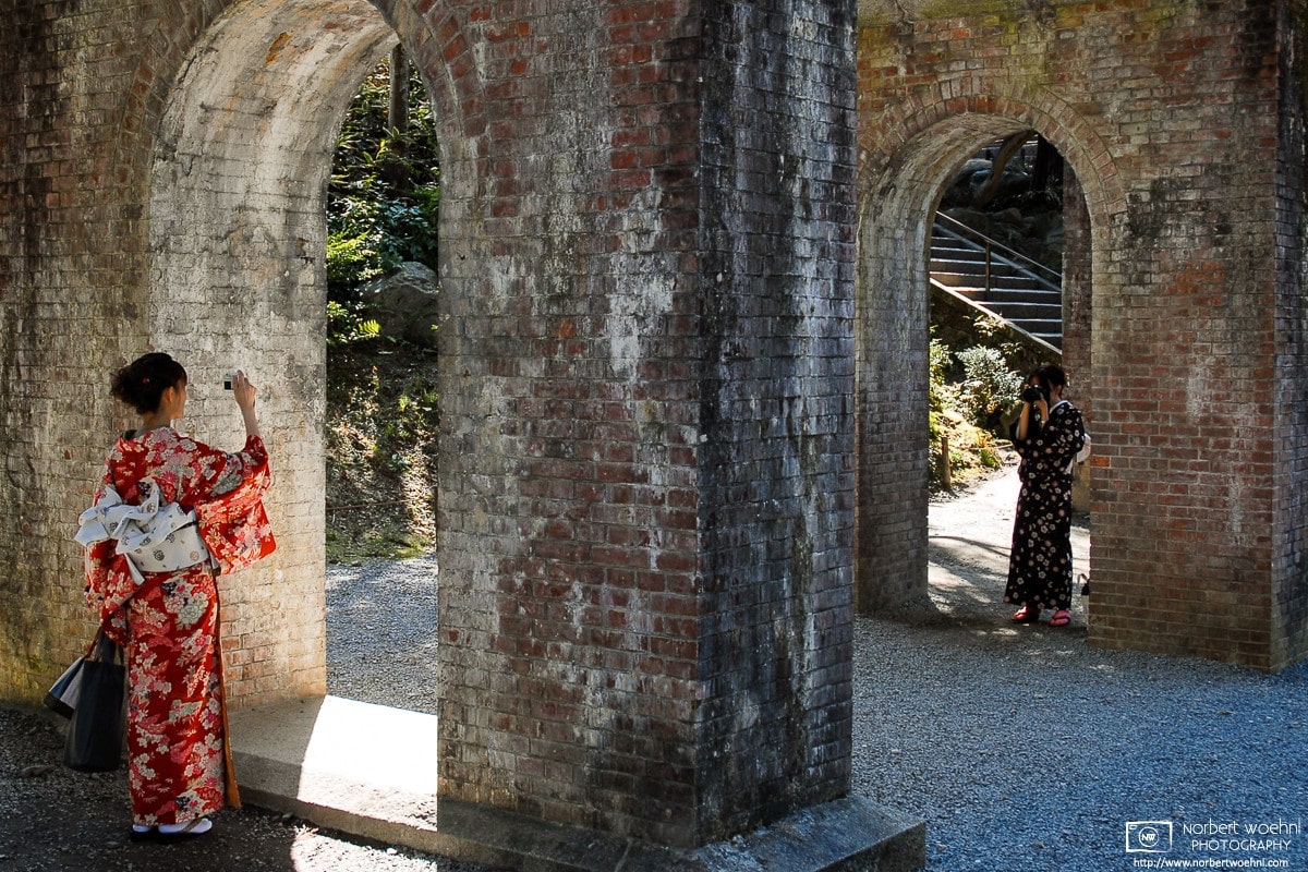 At Nanzenji Temple in Kyoto, Japan, two kimono-clad women are taking photos of each other underneath the arches of a brick-stone aqueduct. © 2006 Norbert Woehnl Photography.