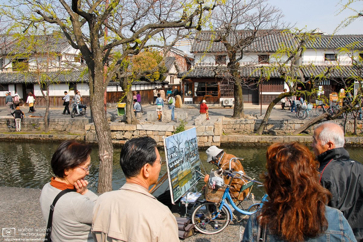 In the historic Bikan district of Kurashiki in Okayama Prefecture, Japan, passersby are watching a painter capture a scene of old buildings along the canal. © 2009 Norbert Woehnl Photography.