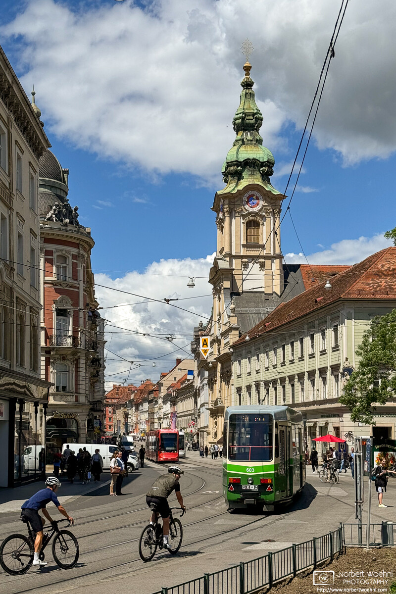 The spire of the City Parish Church (Stadtpfarrkirche) is seen from Am Eisernen Tor in Graz, Austria. © 2024 Norbert Woehnl Photography.