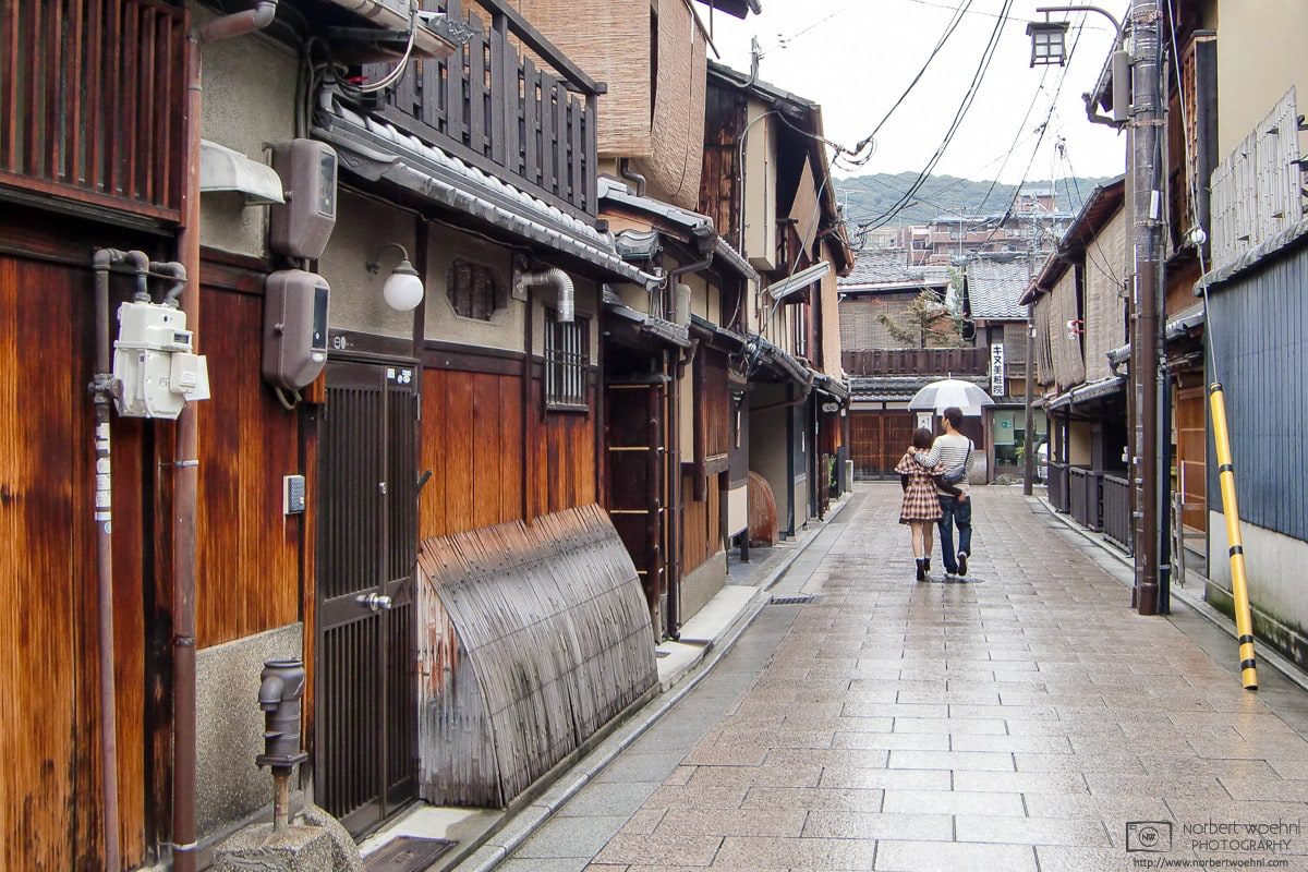 A man and a woman are walking through a side street of the Gion district in Kyoto, Japan, sharing an umbrella during rainy weather. © 2011 Norbert Woehnl Photography.
