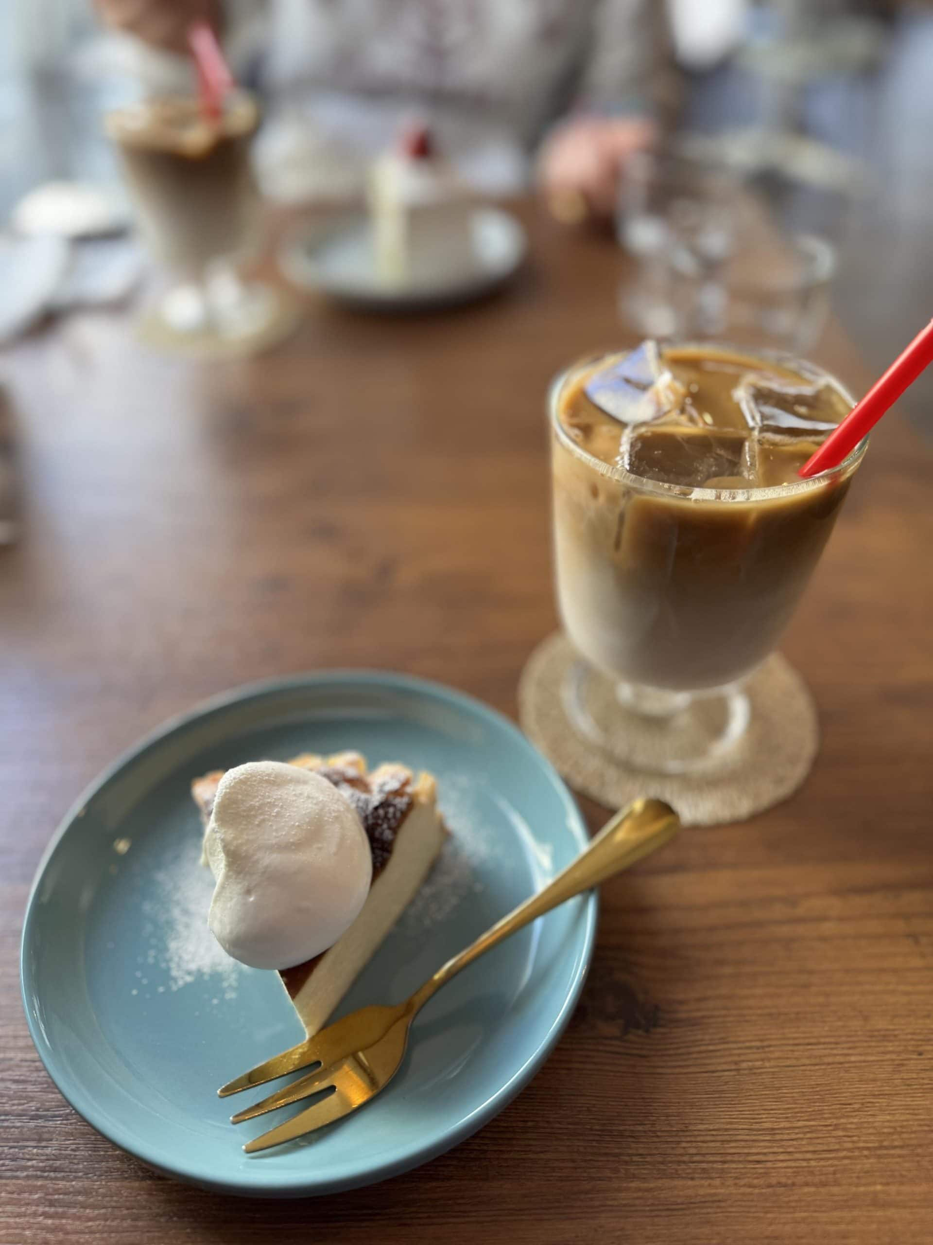 An iced caffe latte and a slice of Basque cheesecake with a topping of whipped cream. © 2026 Norbert Woehnl Photography.