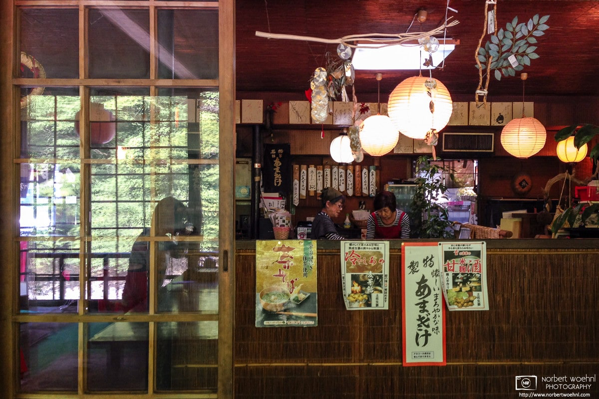 At a noodle restaurant in Takao north of Kyoto, Japan, an interior reflection from a glass door is seen together with the proprietors who are working behind a counter. © 2014 Norbert Woehnl Photography.