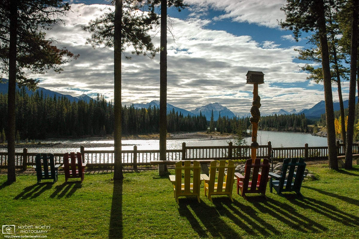At a lodging facility in Jasper National Park, Alberta, colorful deck chairs are facing a bend of the Athabasca River. Mount Kerkeslin is visible in the distance. © 2005 Norbert Woehnl Photography.