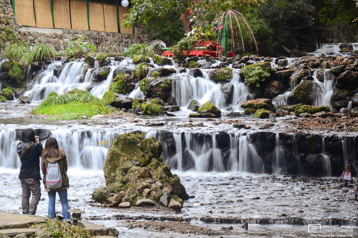 A man and a woman are seen from behind watching and photographing the Kibune River Cascades in northern Kyoto, Japan. © 2011 Norbert Woehnl Photography.
