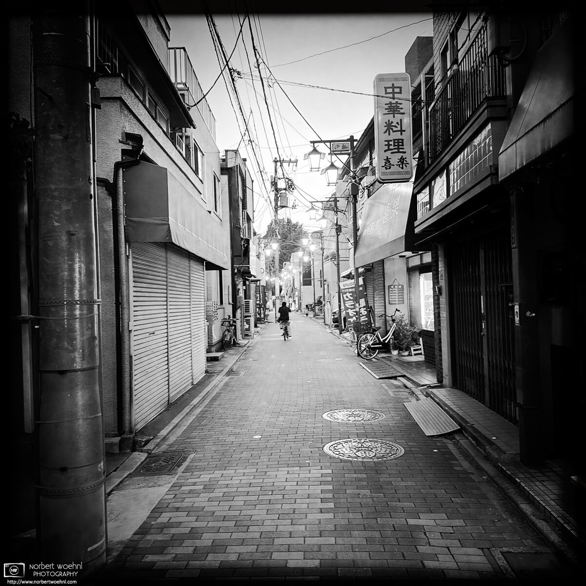 Monochrome evening scene from Inari-dori Shopping Street in the Miyamotocho area of Itabashi Ward in Tokyo, Japan. © 2025 Norbert Woehnl Photography.