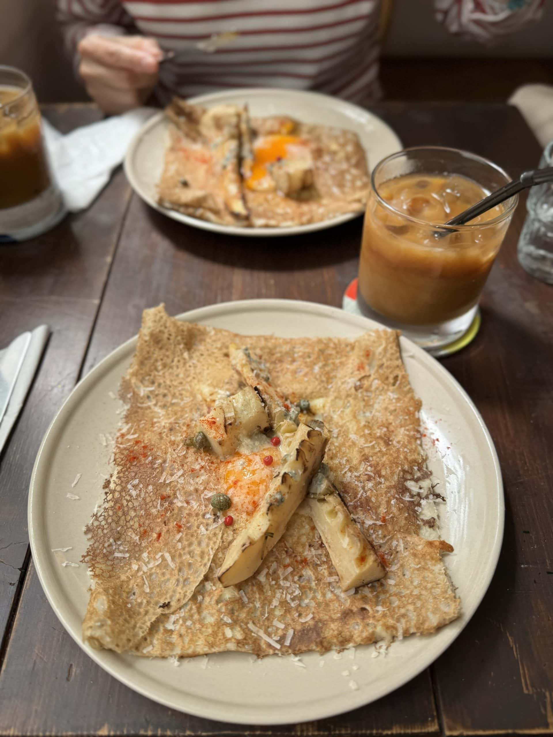Buckwheat galette with bamboo shoots, blue cheese, egg, ham, and a glass of iced coffee. © 2026 Norbert Woehnl Photography.